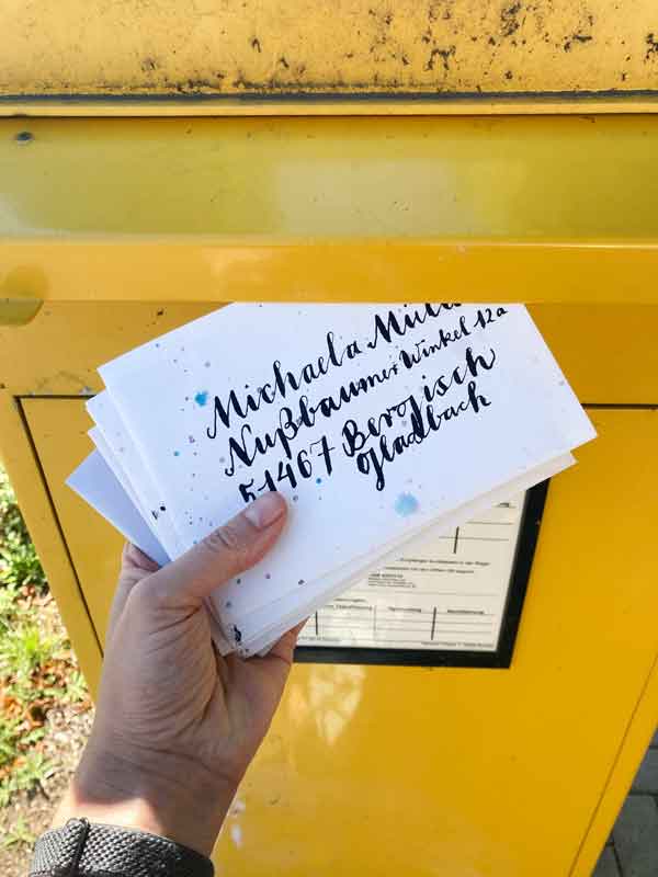 Tabea Heinicker wirft die Sommerpost in einen gelben Briefkasten. Die Sonne scheint.