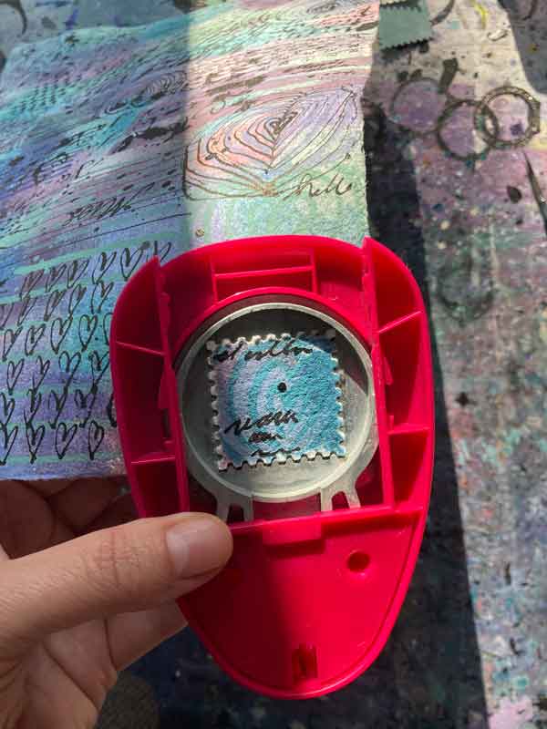 Tabea Heinicker stanzt mit einem Gerät Briefmarken aus dem gemusterten Bogen. Für den MIttwochsMix entstehen Marken.