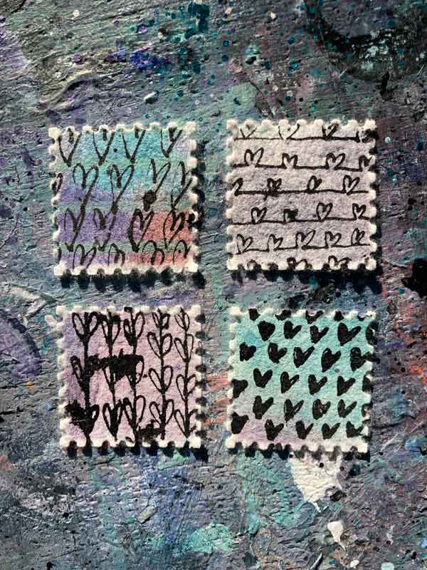 Verschiedene Herzmuster aus der Herzensarbeit von Tabea Heinicker. Vier selbstgestaltete Briefmarken liegen auf einer bunten Tischplatte.