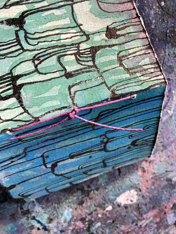 Das fertig gebundenen Büchlein: man sieht die Bindung mit lila Garn am Rücken. Einfache Fadenheftung mit Knoten außen.