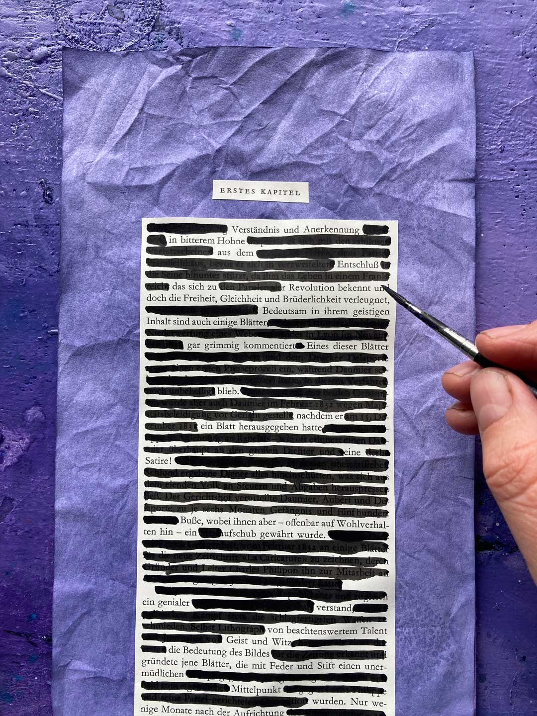 Tabea übermalt Textpassagen auf der Collage mit schwarzer Tusche. Ihre Hand ist zu sehen und der Pinsel.
