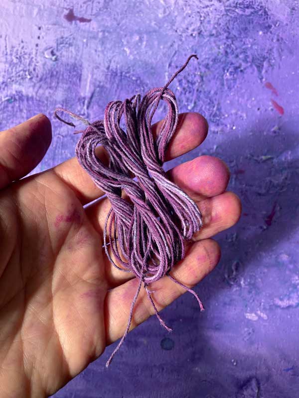 Tabeas bunte Hand mit den fertigen Garnen. Sie sind Lila gesprenkelt.