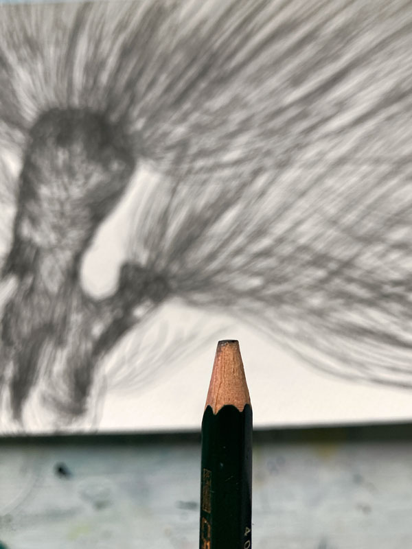Abgenutzter Bleistift im Vordergrund. Hinten liegt eine Zeichnung mit Baum.