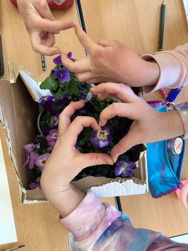 Von den Kindern lernen: Zwei Kinder halten ihre Hände über unser Motiv Veilchen im Topf. Sie formen Herzen aus ihren Fingern, denn sie freuen sich über das Motiv.
