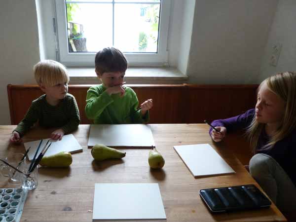 Drei Kinder sitzen am Tisch und zeichnen Birnen. Die Aquarellpapiere sind noch leer.
