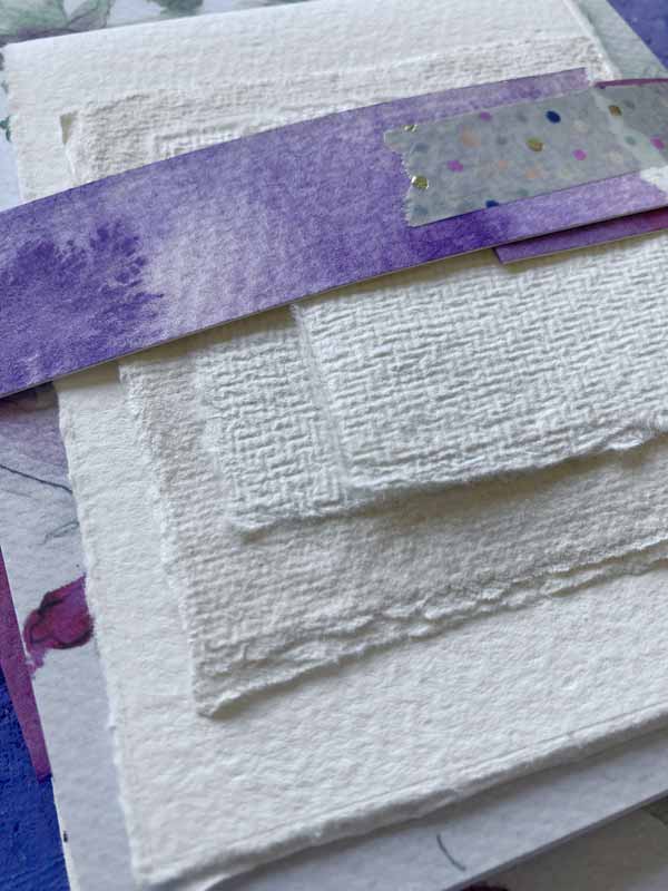 Bündel mit unterschiedlichen Aqaurellpapieren und Postkarten, die zum Buch gelegt werden.