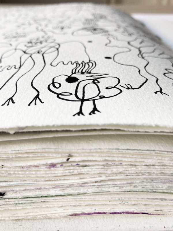 Skizzenbuch im Halbprofil. Man sieht die Seiten des Buches, es ist fast voll. Oben erkennt man einen kleinen kecken Tuscheengel.